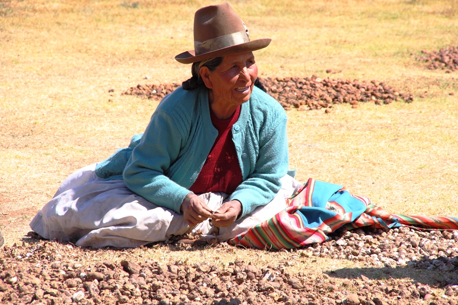Alte Frau mit sonnengegerbter Haut mit Hut sitzt in farbigem Gewand am Boden