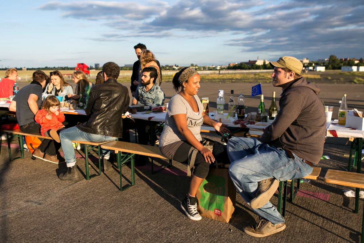 Im Abendlicht sitzen junge Menschen verschiedener Ethnien im Freien an einem Tisch