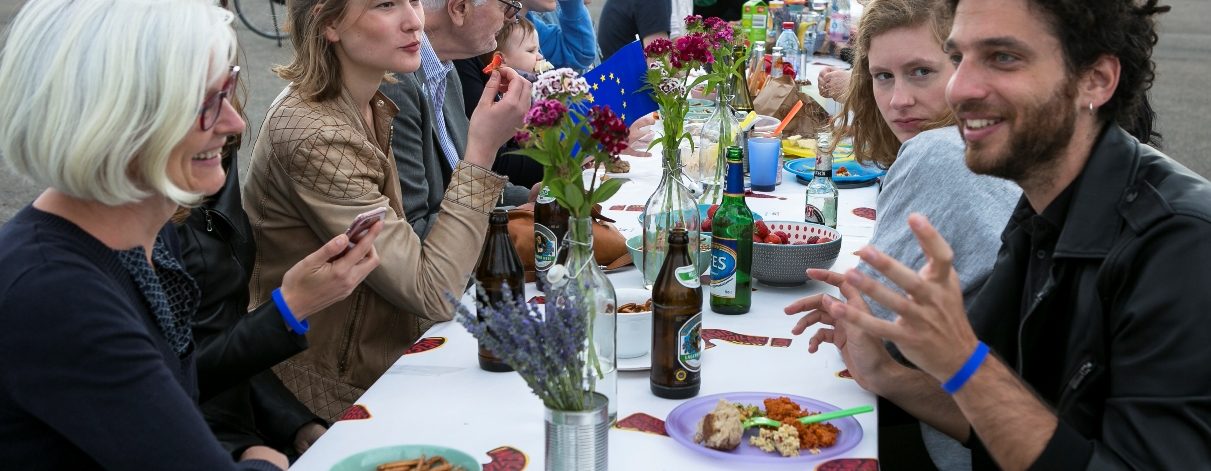 Personen verschiedenster Altersstufen sitzen im Freien an einem Tisch