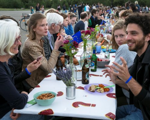 Personen verschiedenster Altersstufen sitzen im Freien an einem Tisch