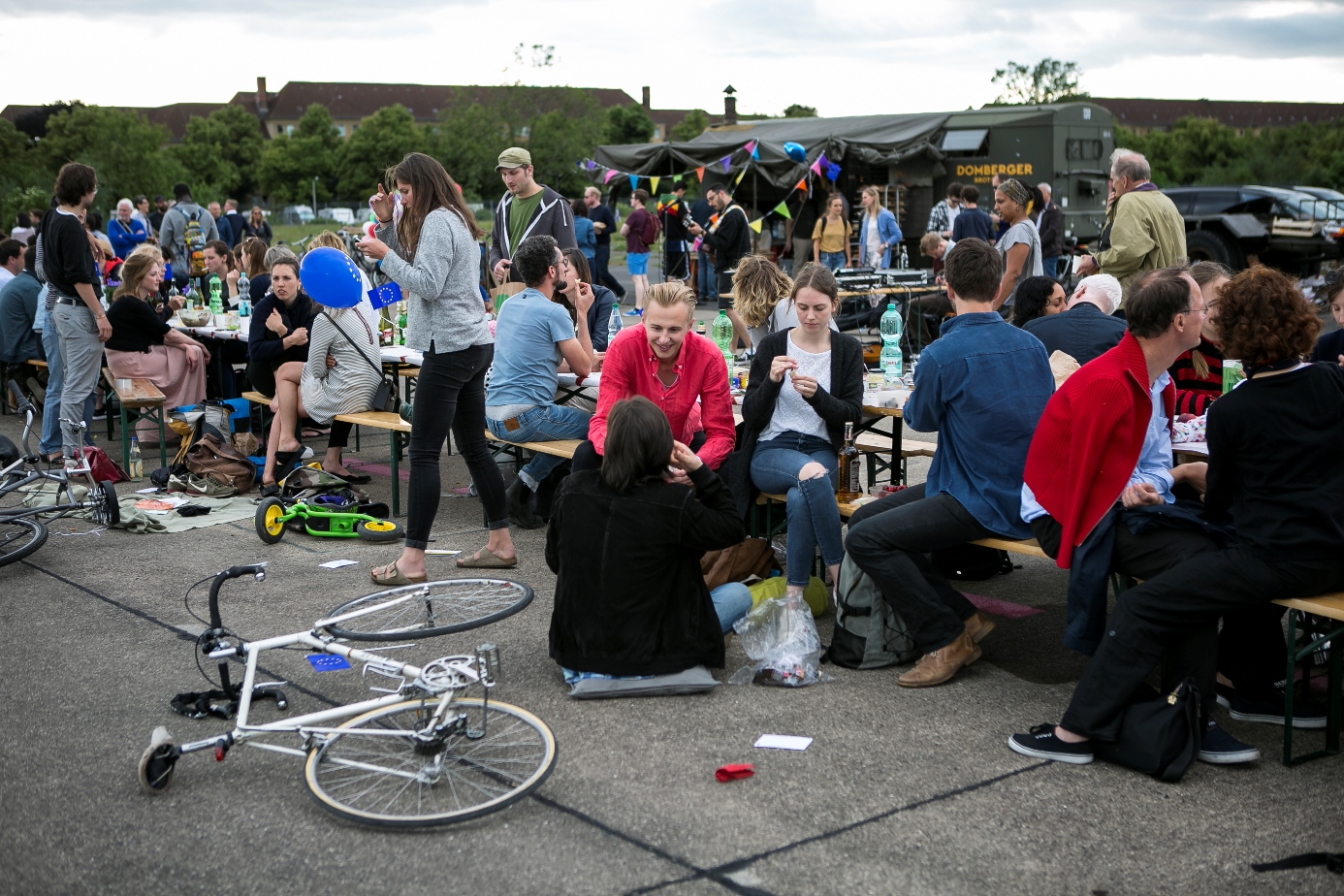 Großes Fest mit Tischen im Freien, Räder liegen am Boden, junge Menschen unterhalten sich