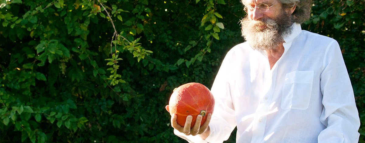 Mann mit Rauschebart und lockigem Haar hält Kürbis in der Hand und betrachtet ihn