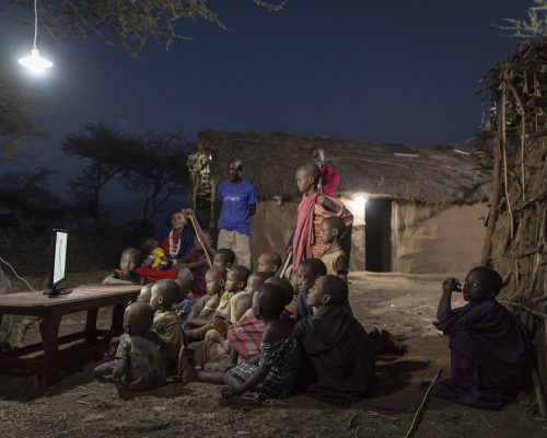 Eine Gruppe schwarzer Kinder sitzt im Freien im Dunkeln vor einem Fernseher