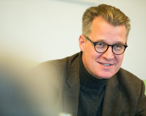 Mann mittleren Alters mit braungrauem Haar und runder Hornbrille