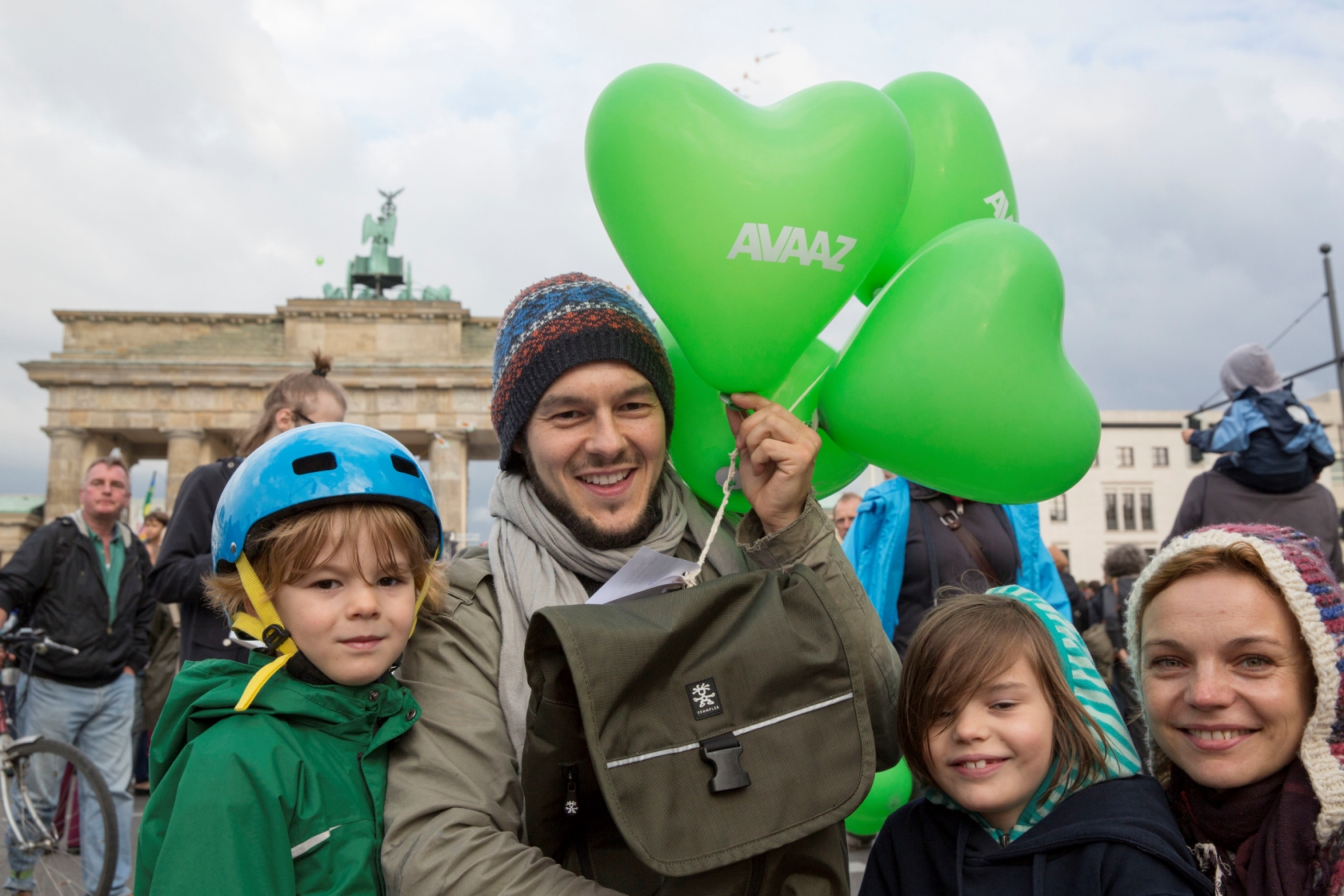 Zwei Kinder, ein Mann und eine Frau stehen vor dem Berliner Tor und halten Herzluftballone in grün mit der Aufschrift AVAAZ