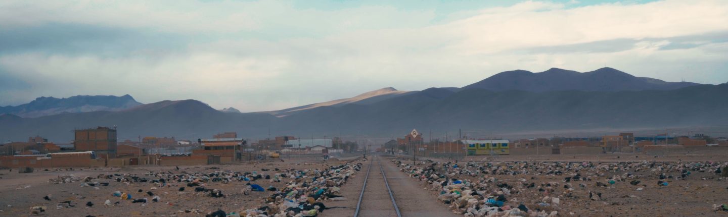 Blick auf hohe Berggipfel, im Vordergrund eine gerade Eisenbahnschiene gesäumt von Plastikmüll