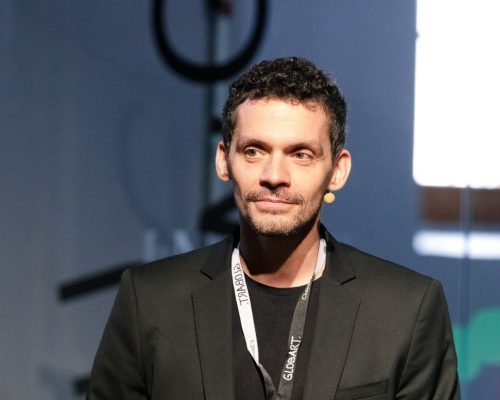 Mann in Anzug kurzen Haaren und getrimmtem Bart steht auf einer Bühne