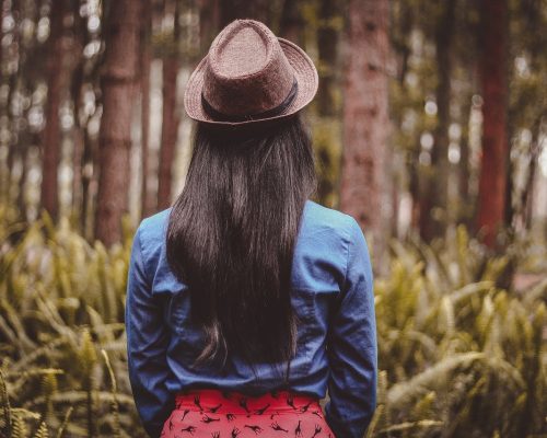 Frau mit Hut blickt in Wald