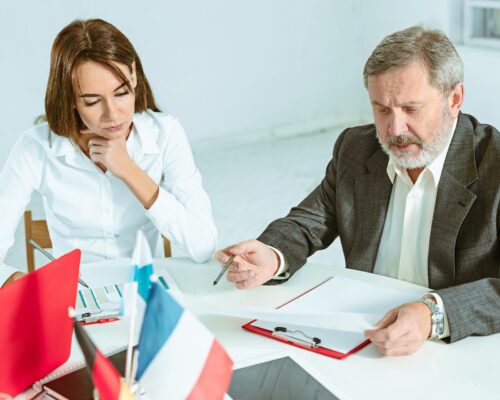 2 Personen sitzen an Tisch und sichten Zettel