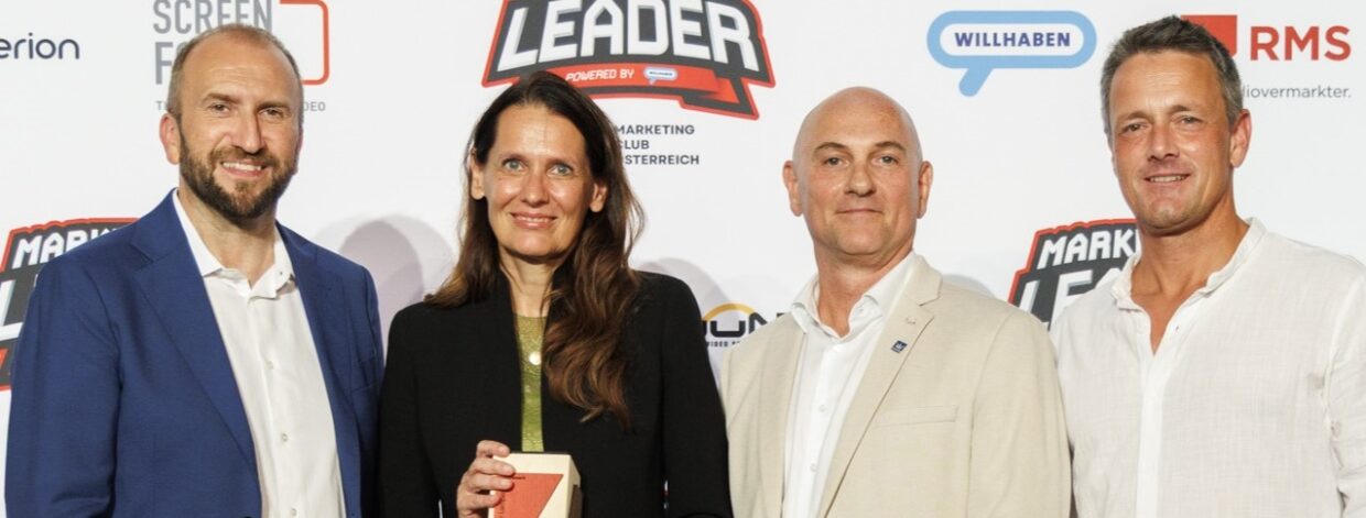 4 Personen lächeln in die Kamera und halten Preis aus Holz in der Hand